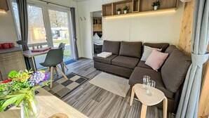 A modern living room with a sofa, a small table, a dining area with a chair, and a kitchen area with a counter and cabinets. - Tiny Haus Benjamin by Interhome (Beilngries)