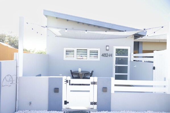 A modern building with a white exterior, a number '482-H' on the wall, and a gated entrance. - Cozy 1-bedroom apartment in great Palm Beach with AC, WiFi and private pool. (Noord)