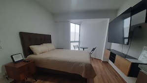 A bedroom with a bed, bedside table, TV, and a view of the outdoors. - Mini loft in front of malecon Bertolotto (minutes from Costa 21 and airport) (San Miguel)