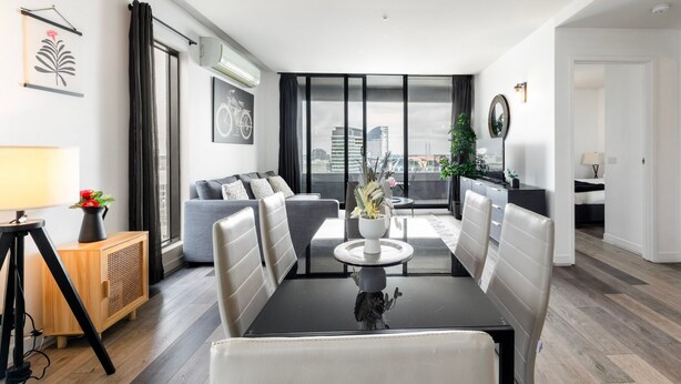 A modern living room with a dining area, a sofa, a TV, and a balcony with a city view.