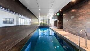 A modern indoor swimming pool with a clear view of the surrounding area, including a TV screen and a sign indicating the pool's location.