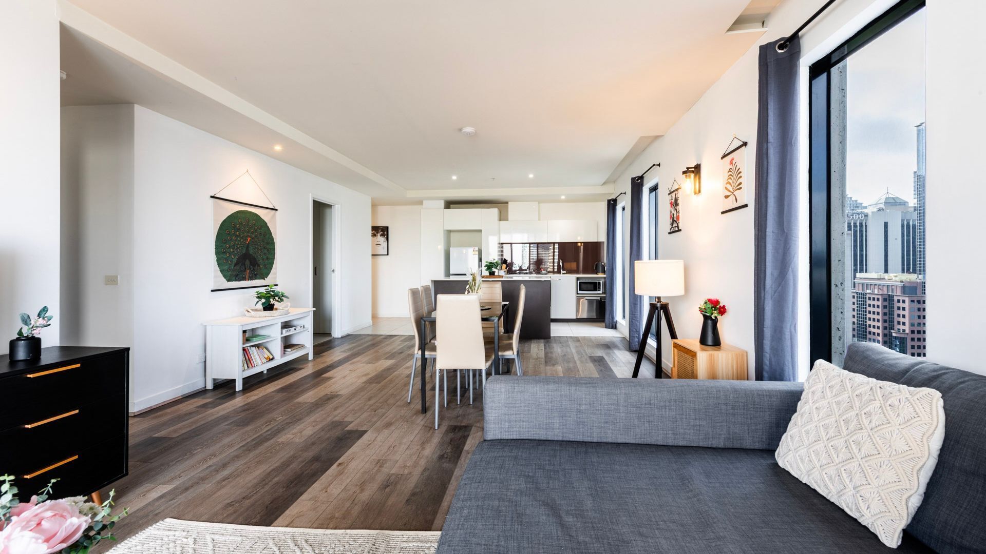 Una sala de estar moderna con un sofá gris, un comedor y una cocina.