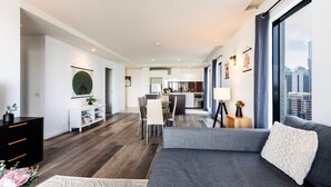 A modern living room with a grey sofa, a dining area, and a kitchen.