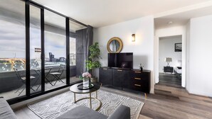 A modern living room with a large sliding glass door, a black entertainment unit, a round mirror, and a view of the cityscape.