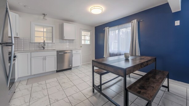 A modern kitchen with white cabinets, a stainless steel dishwasher, and a wooden table with a bench. - Dune's Edge Retreat Peaceful home near State park and trails (South Haven)