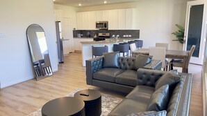 A modern living room with a sectional sofa, two round side tables, and a kitchen in the background.