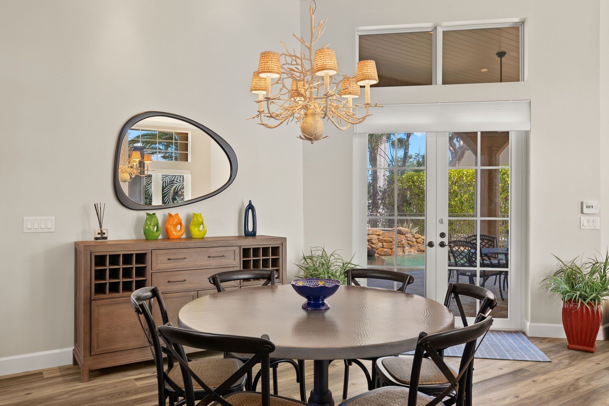 A dining area with a round table, chairs, a chandelier, a mirror, and a cabinet with decorative vases.