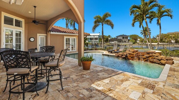 An outdoor pool area with a patio table and chairs, surrounded by palm trees and a view of a lake. - Spectacular Direct access canal front beauty! (Sanibell)
