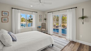 A bedroom with a bed, a ceiling fan, a view of a swimming pool, and a door leading to an outdoor area. - Spectacular Direct access canal front beauty! (Sanibell)