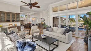 A spacious living area with a large sofa, coffee table, and a ceiling fan. There is a kitchen in the background with cabinets and a dining area. - Spectacular Direct access canal front beauty! (Sanibell)