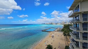 A beach with clear blue water, a pier, and a city skyline in the background. - Beachfront 8th Floor Sans Souci Studio - 30 Day Rental (Honolulu)