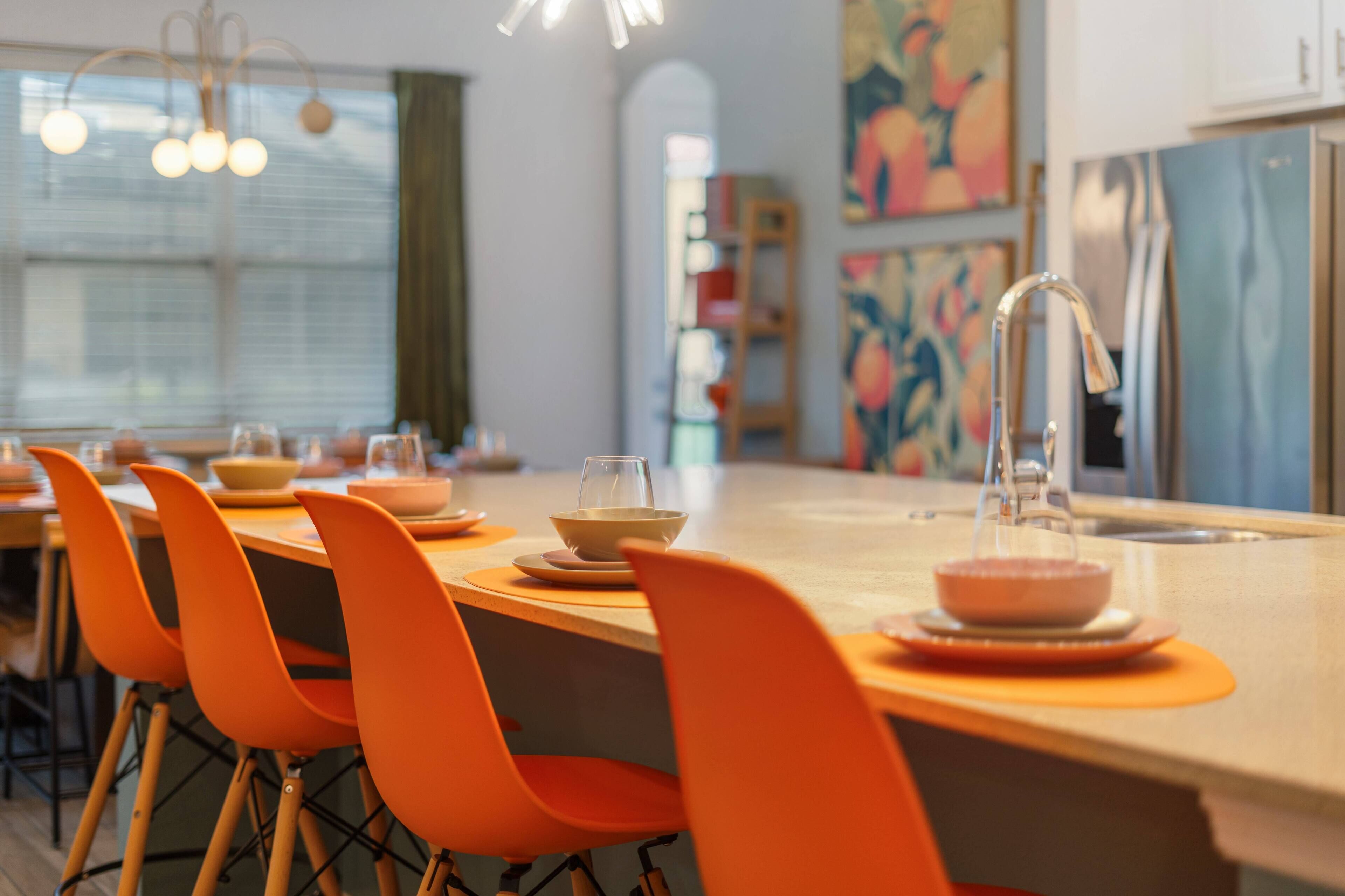 Une cuisine moderne avec un îlot central, des chaises orange et un évier en acier inoxydable.