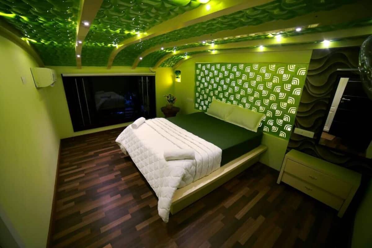 Un dormitorio con piso de madera, una cama con colchón verde, un televisor montado en la pared y un panel decorativo.