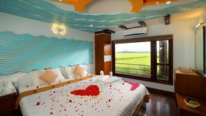A hotel room with a large bed, a view of a green field, and a decorative ceiling. - Marvelous Boathouse (Alappuzha)