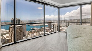 A high-rise room with large windows offering a city view, a bed, and a view of a marina.