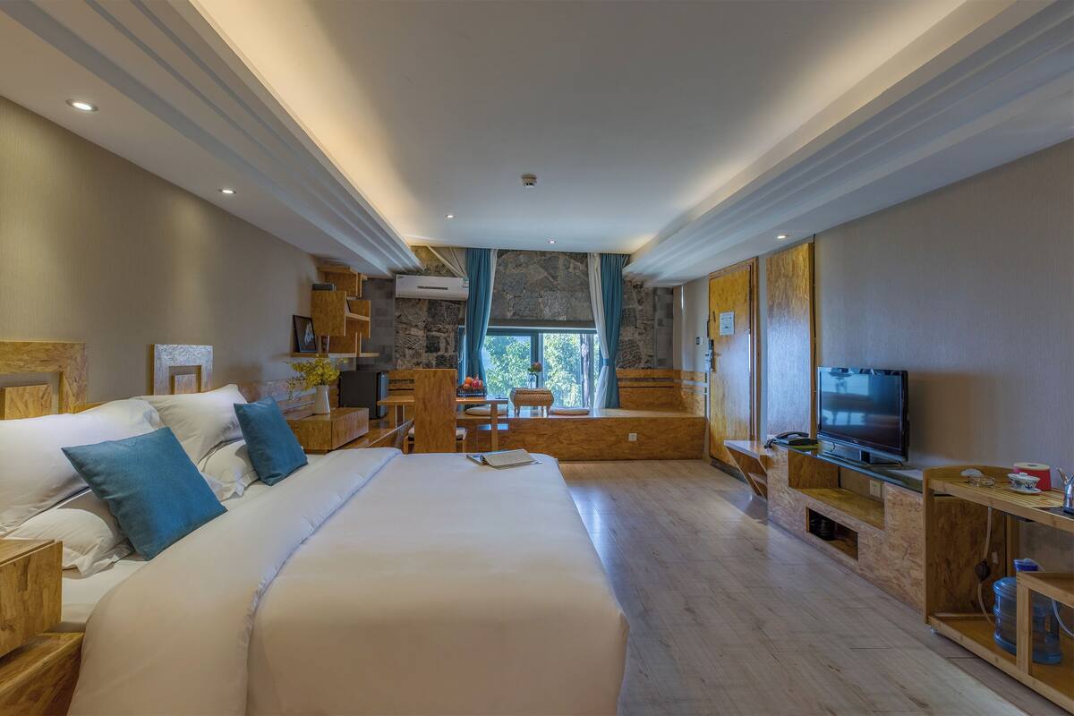 Una habitación de hotel moderna con una cama grande, cabecera de madera, televisor y una pared de acento de piedra.
