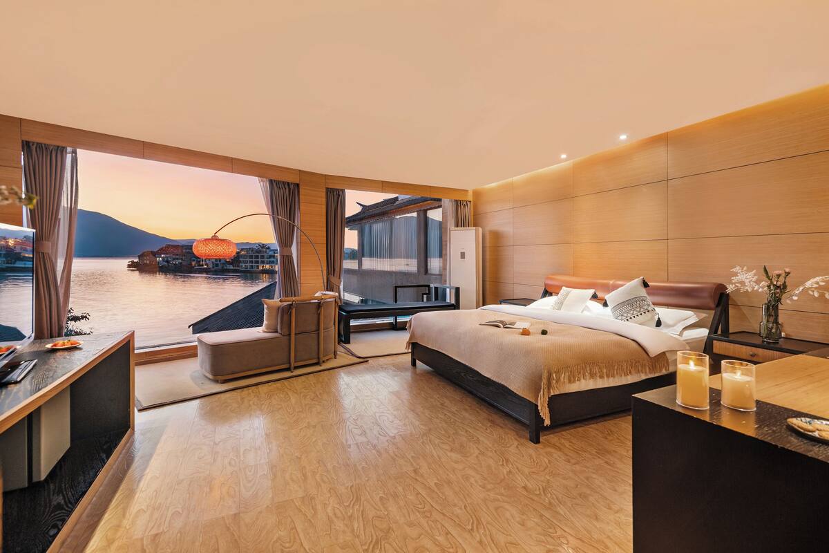Habitación de hotel moderna con una cama grande, un escritorio y vistas al agua y a las montañas.