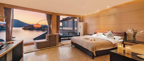 Habitación de hotel moderna con una cama grande, un escritorio y vistas al agua y a las montañas.
