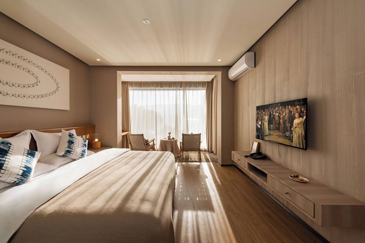 Una habitación de hotel moderna con una cama grande, una mesita con sillas, un televisor y un cuadro en la pared.