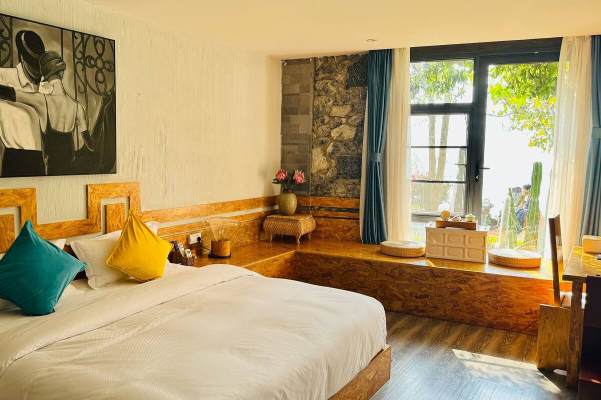 Habitación de hotel con cama, un cuadro, pared de piedra, ventana con cortinas y vistas a zonas verdes.
