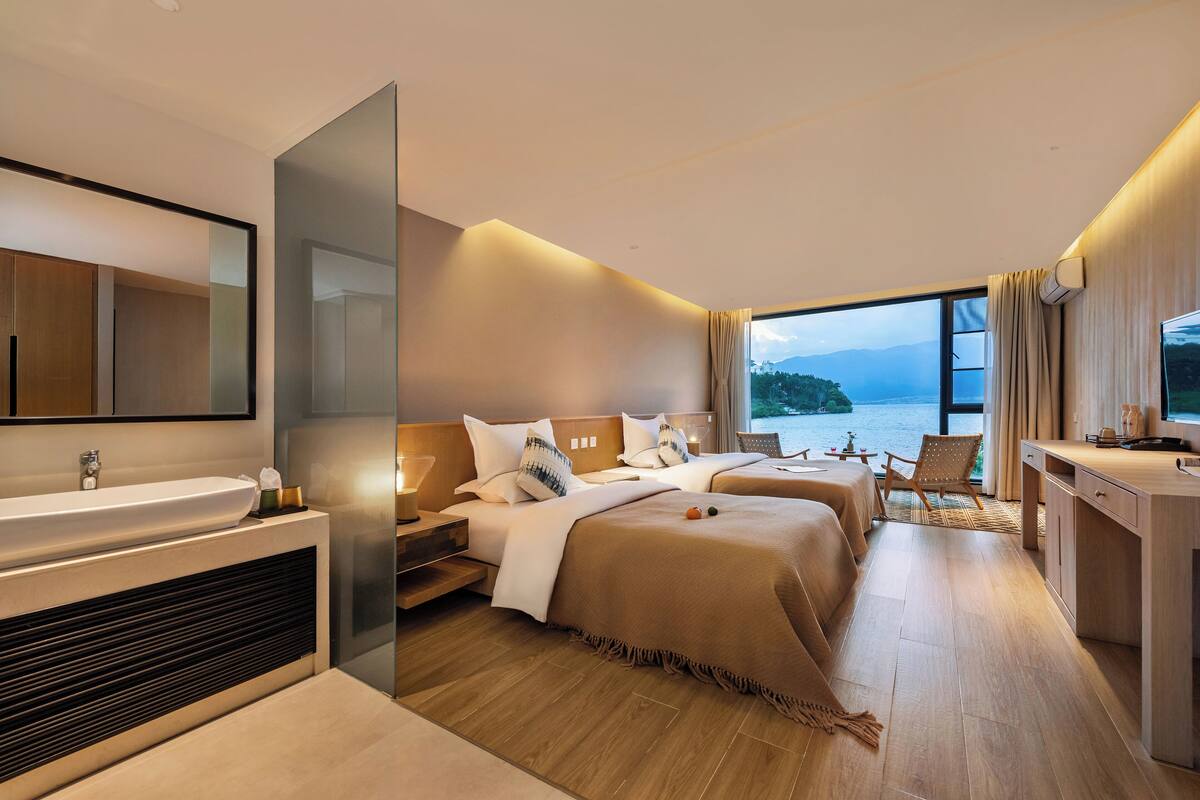 Habitación de hotel moderna con una cama grande, un escritorio independiente, un baño con un espejo amplio y vistas al mar.