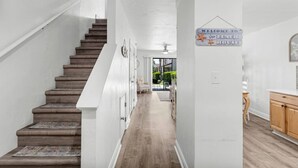 Un interior moderno con una escalera de madera, un pasillo que conduce a un comedor, y un letrero que dice "WELCOME TO the BEACH HOUSE".