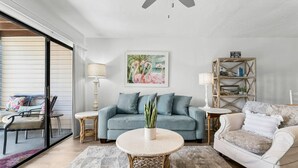 Una sala de estar con un sofá azul, un sillón blanco, una mesa de centro redonda y una estantería.