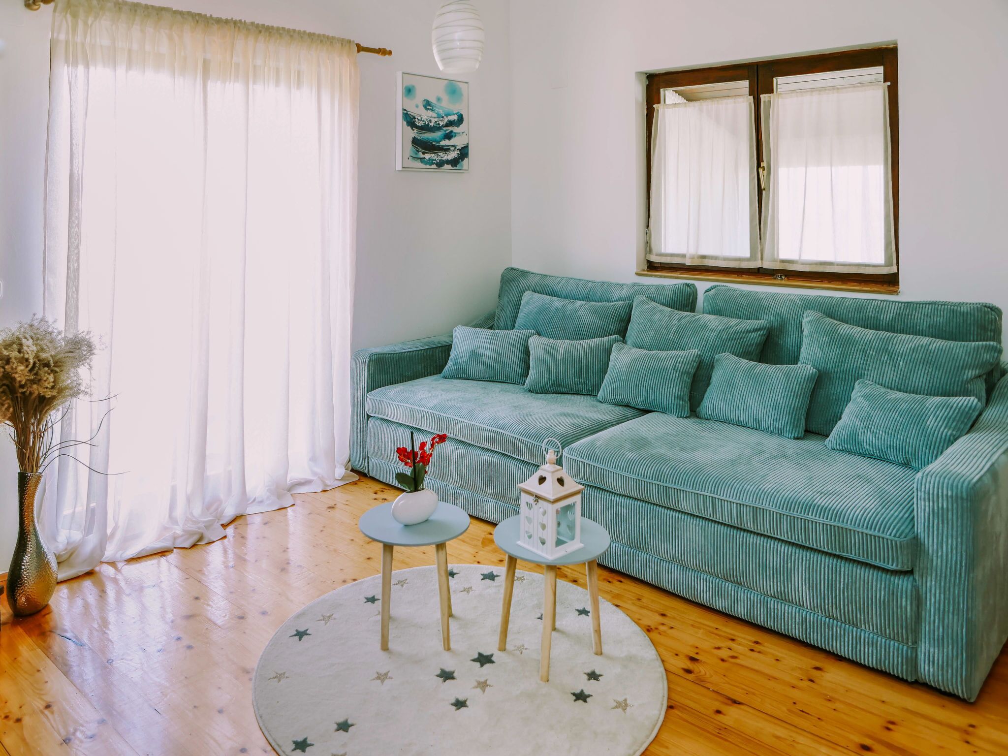 A living room with a green sofa, a small round table, a vase with flowers, a star-patterned rug, and a painting on the wall.