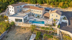 Una casa grande de varios pisos con piscina, fachada de piedra y jardín.