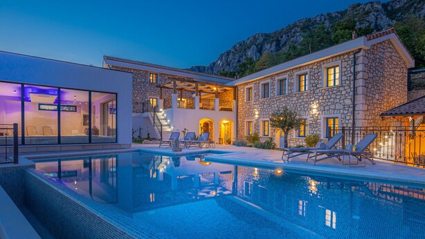 Una villa moderna con piscina, fachada de piedra y vistas a las montañas.