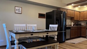 Een eetruimte met een houten tafel en stoelen, een kroonluchter en een keuken op de achtergrond.