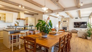 Une cuisine spacieuse avec des poutres en bois, un coin repas avec une table et des chaises en bois, et un salon avec un canapé et un téléviseur.