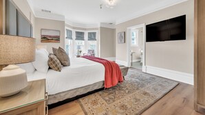 Un dormitorio con cama, televisor, lámpara y vista al exterior.