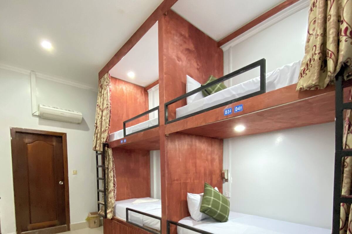 Habitación con literas de madera, una puerta y un equipo de aire acondicionado.