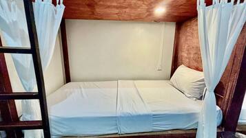 Una cama individual en literas con ropa de cama blanca, cabecera de madera y cortinas blancas.