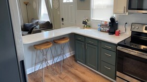 A kitchen with a refrigerator, stove, and bar stools. - Cottage on Main st- Low Cleaning Fee (Saint Charles)