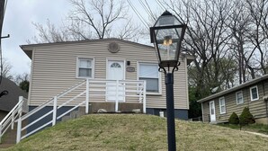 A two-story house with a front porch, a stone retaining wall, and a black street lamp. - Cottage on Main st- Low Cleaning Fee (Saint Charles)