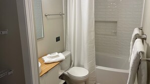 A bathroom with a toilet, a shower with a white curtain, a bathtub, and a towel rack. - Cottage on Main st- Low Cleaning Fee (Saint Charles)
