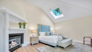 A bedroom with a fireplace, a bed with a headboard, a bench, and a skylight.