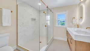 A modern bathroom with a glass-enclosed shower, a white toilet, and a vanity with a mirror.