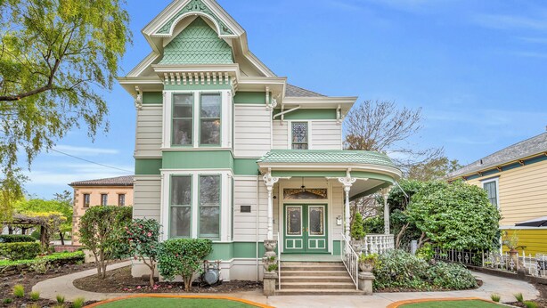 A two-story Victorian-style house with a green and white facade, a front porch, and a well-maintained garden.