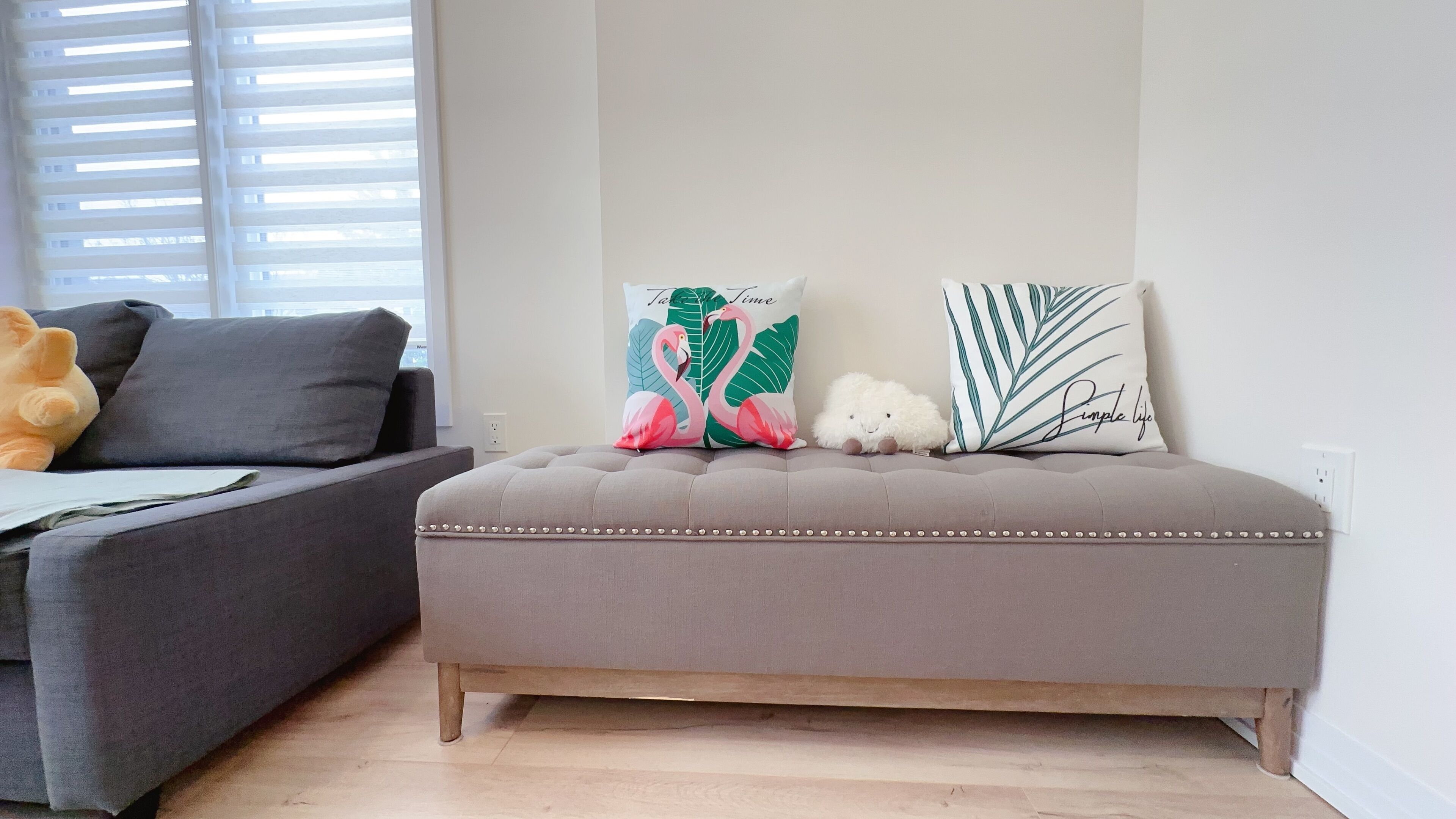 A living room with a grey sofa, a grey ottoman, and two decorative pillows with floral designs.