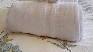Een net opgemaakt bed met opgerolde handdoeken, een sprei met bloemenmotief en een wit metalen hoofdeinde.