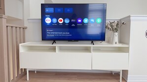 Een flatscreen televisie op een wit tv-meubel met diverse app-icoontjes, waaronder Netflix en YouTube.