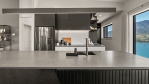 Une cuisine moderne dotée d’un grand îlot central, d’appareils électroménagers en acier inoxydable et offrant une vue sur un lac.