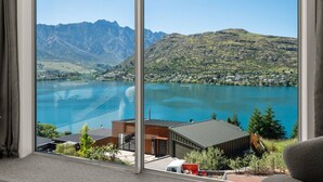 Une pièce dotée d’une grande fenêtre donnant sur un lac, des montagnes et un petit bâtiment.