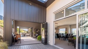 Une maison moderne dotée d’une terrasse en bois, d’un coin repas et d’une grande porte-fenêtre coulissante donnant sur un balcon.