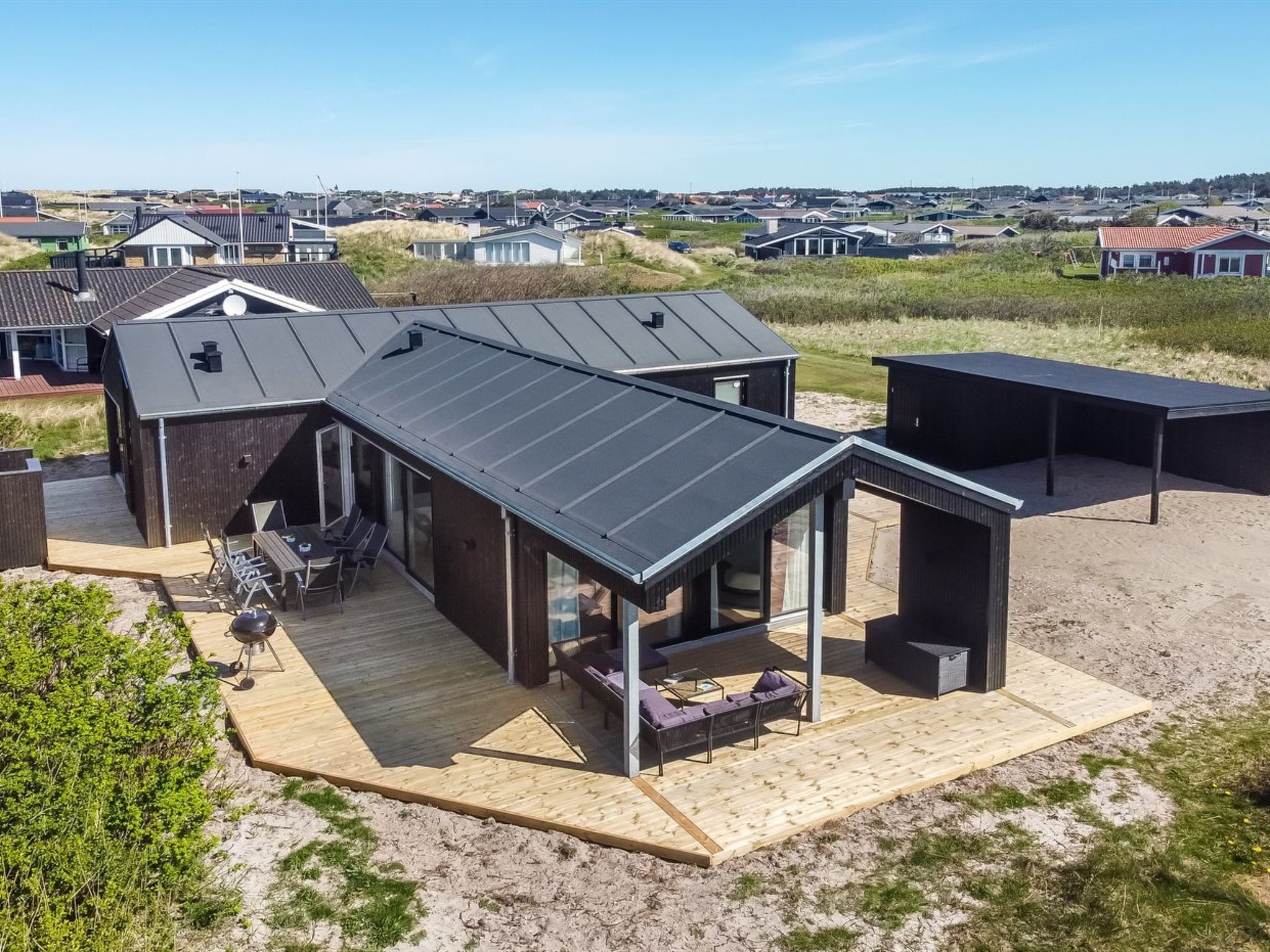 Ein modernes Haus mit einer großen Terrasse, einem überdachten Sitzbereich und Blick auf die umliegende Nachbarschaft.