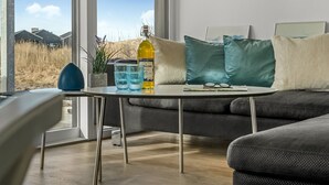 Una sala de estar moderna con un sofá, una mesa de centro y vistas a un campo a través de ventanas amplias.