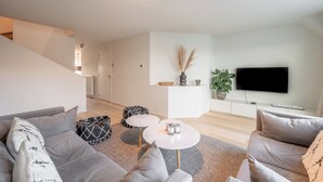 A modern living room with a grey sofa, a coffee table, and a TV mounted on the wall. - Apartment on Belgian Coast Near Beaches (Knokke-Heist)